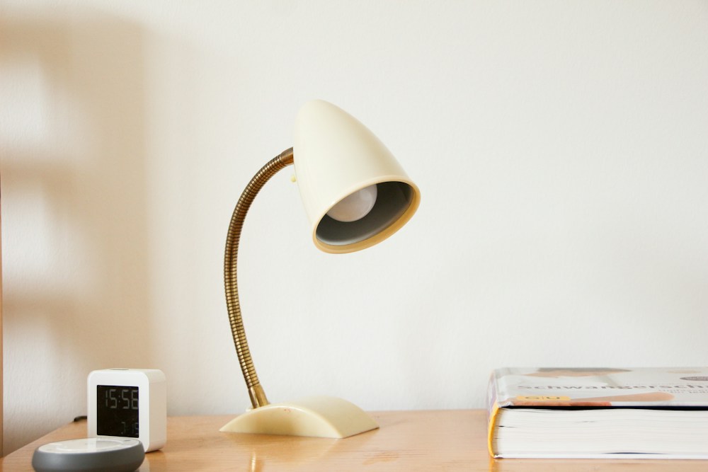 A cream desk lamp with a curved neck on a wooden table